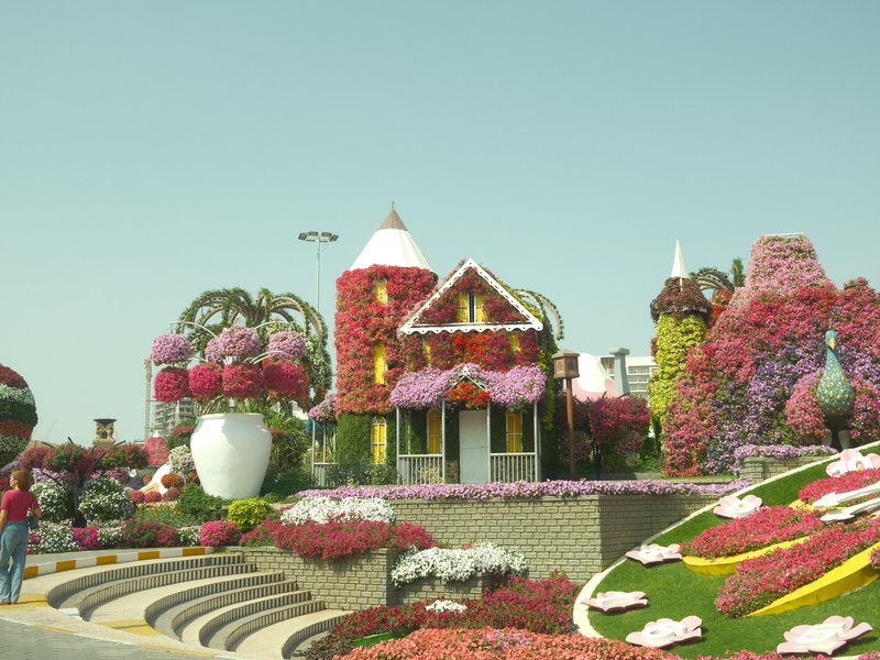 Colorful flower displays surrounding a whimsical house in a garden setting.