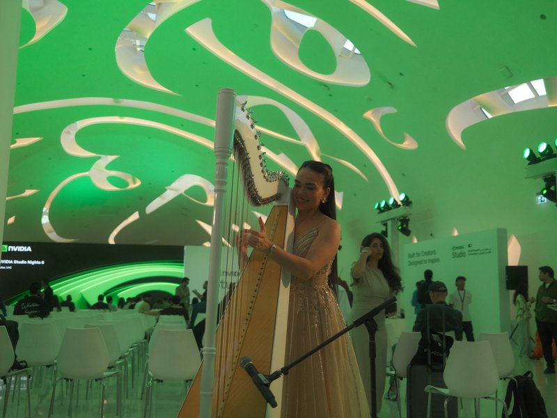 A woman playing a harp under a green, abstract ceiling in a modern indoor setting.
