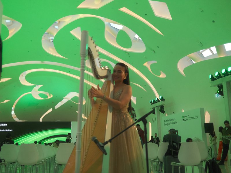 A musician playing a harp in a modern venue with green lighting and a unique ceiling design.