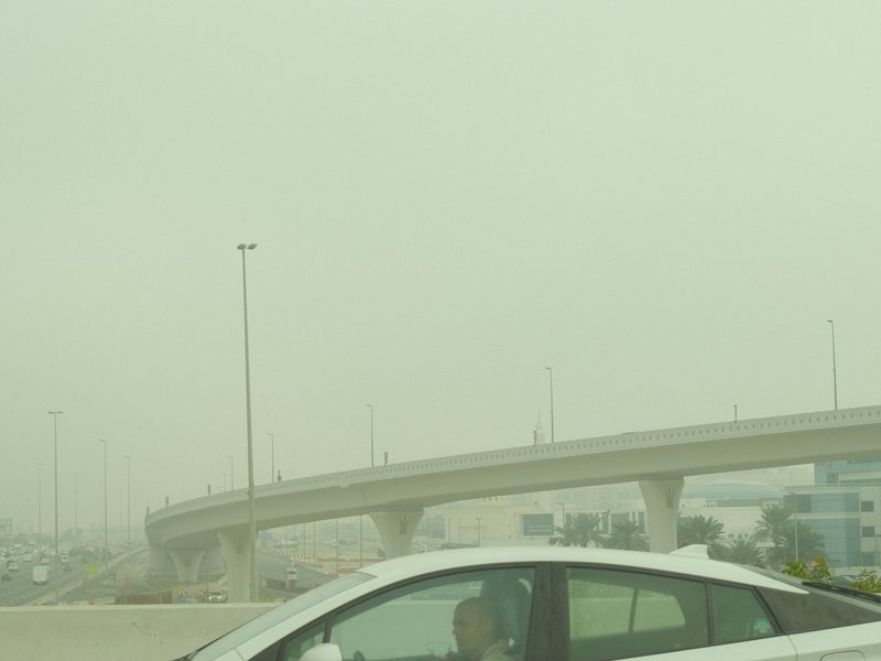 A hazy urban scene featuring a white car on a highway with an overpass in the background.