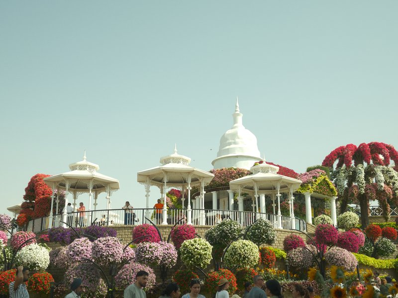A vibrant floral display surrounding a white structure with domes under a clear sky.