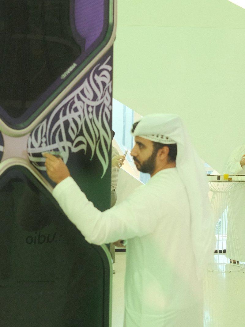 A man in traditional Emirati attire interacting with a modern art installation in a bright indoor space.