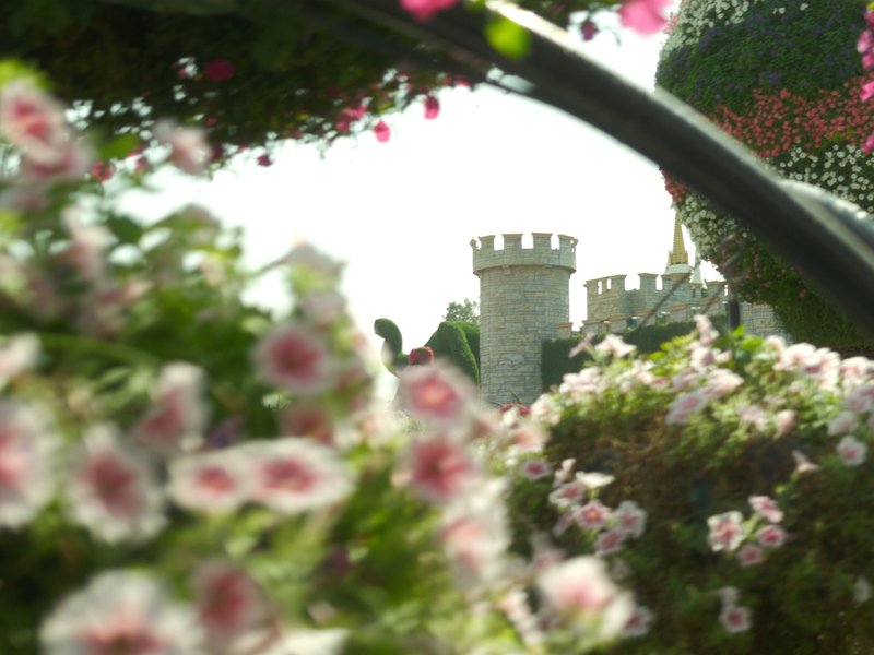 A castle tower partially obscured by colorful flowers in a garden setting.