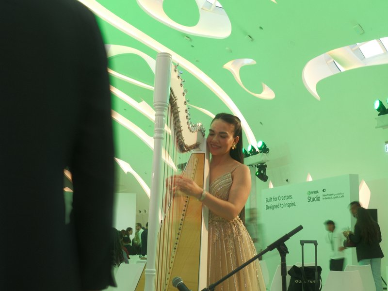 A woman playing a harp in a modern venue with green lighting and abstract ceiling design.