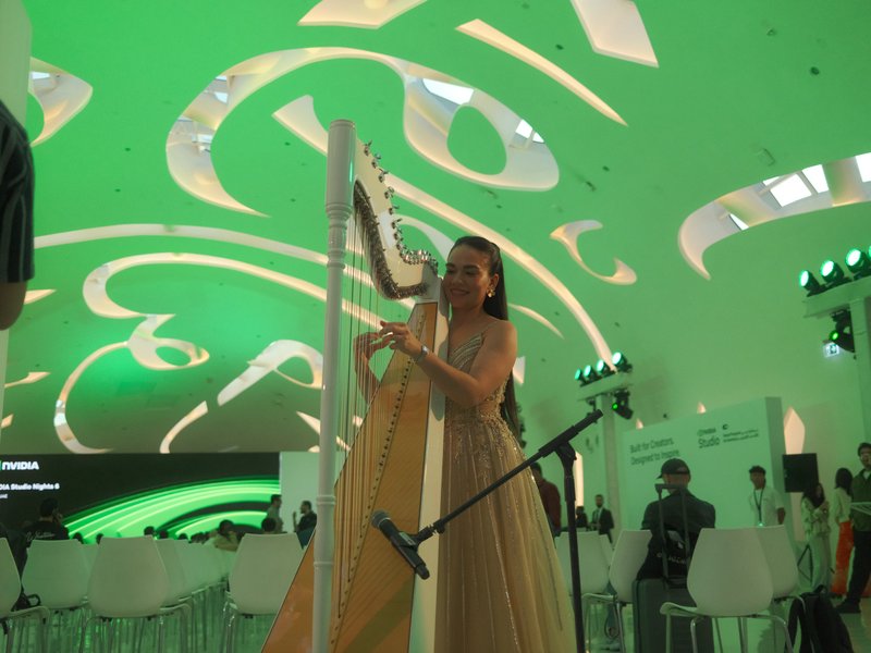A woman playing a harp under a green, abstract ceiling in a modern indoor setting.