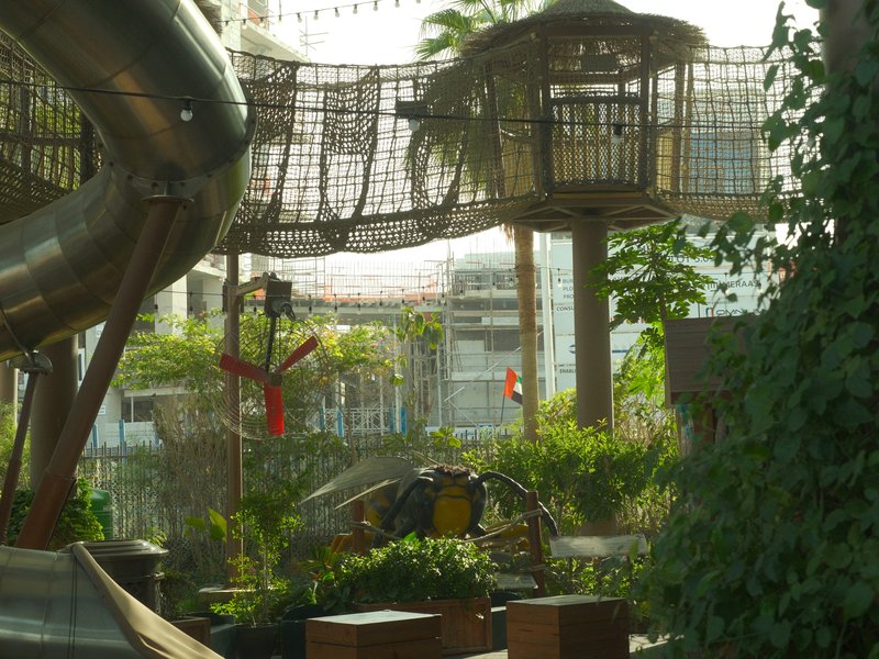 Playground scene featuring a slide, treehouse, and greenery in an urban setting.