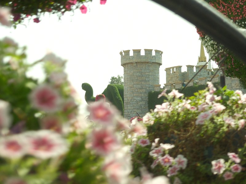 A castle partially obscured by colorful flowers in a bright outdoor setting.