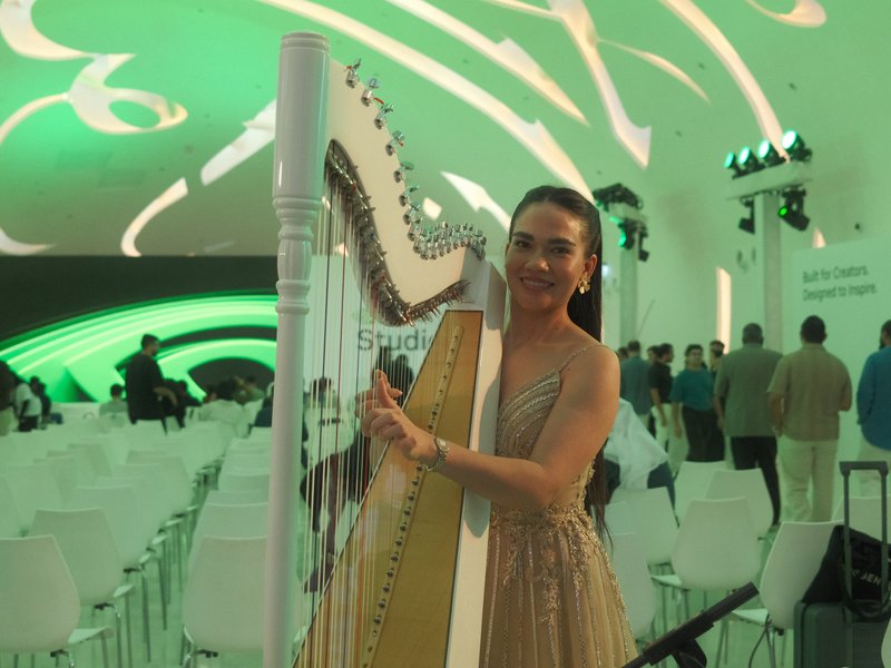 A woman in a shimmering dress poses with a harp in a modern event space with green lighting.