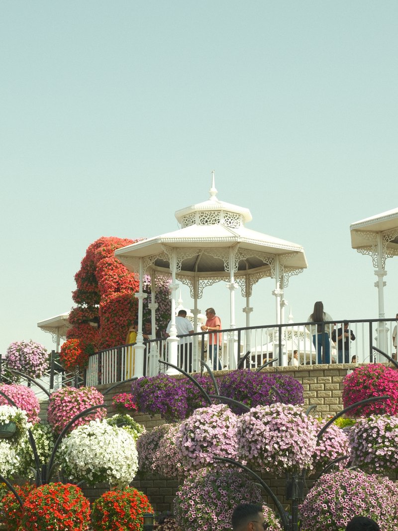 A vibrant garden scene with colorful flowers and a white gazebo, people enjoying the view.