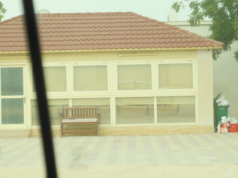 A light-colored building with large windows and a bench in front, set in a hazy environment.
