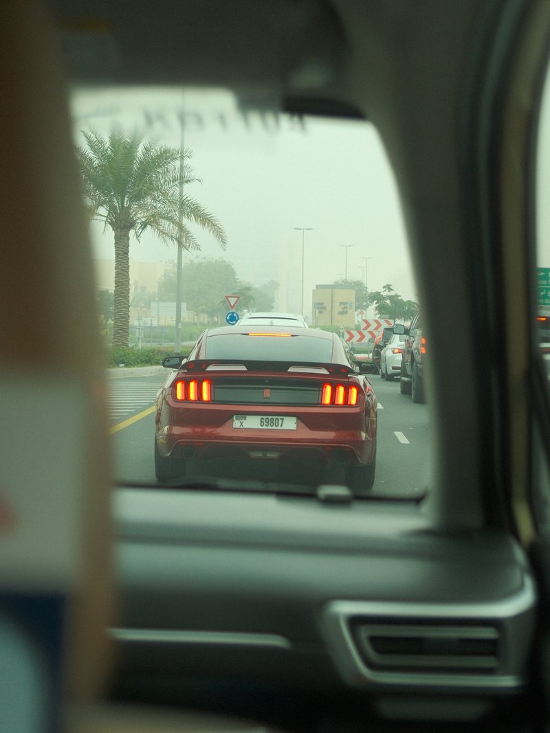 View from a car showing a red Mustang in traffic with palm trees in the background.