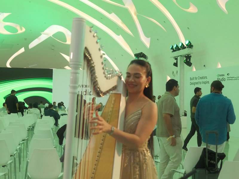 A woman in a shimmering dress poses with a harp in a modern, brightly lit indoor setting.