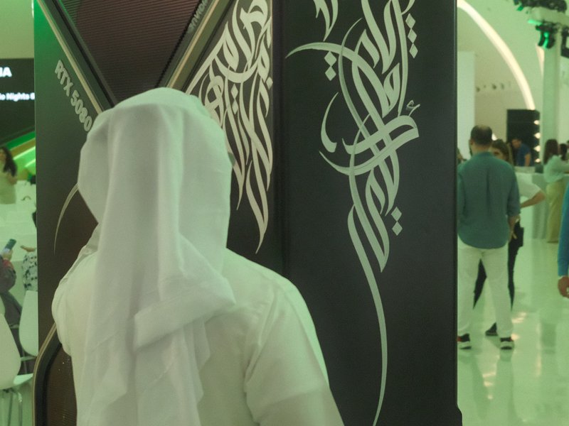 A person in traditional attire stands in front of a decorative wall with intricate patterns in a modern setting.
