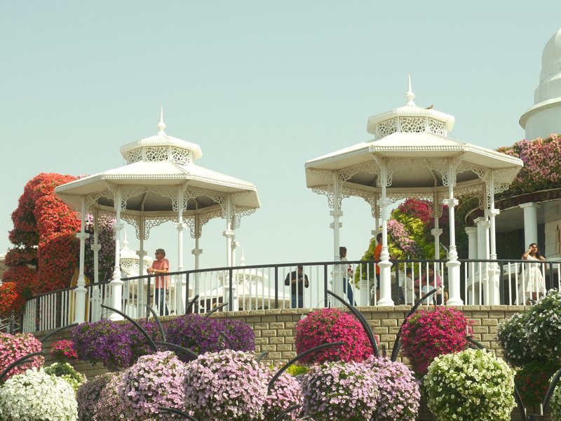 Two white gazebos surrounded by colorful flowers in a bright outdoor setting.