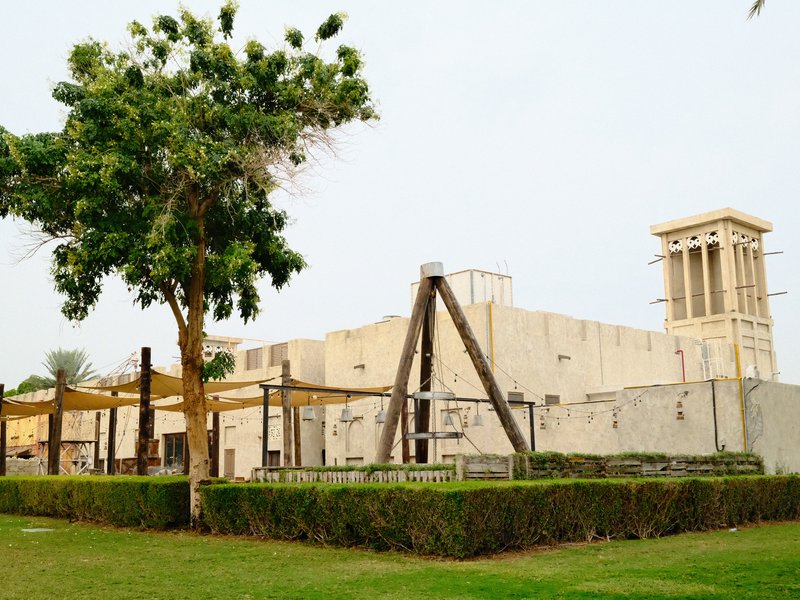 A traditional building with a wind tower, surrounded by greenery and a swing set in a park.