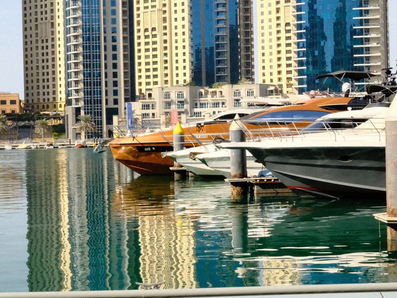 Luxury yachts docked in a marina with tall buildings reflecting in the water.