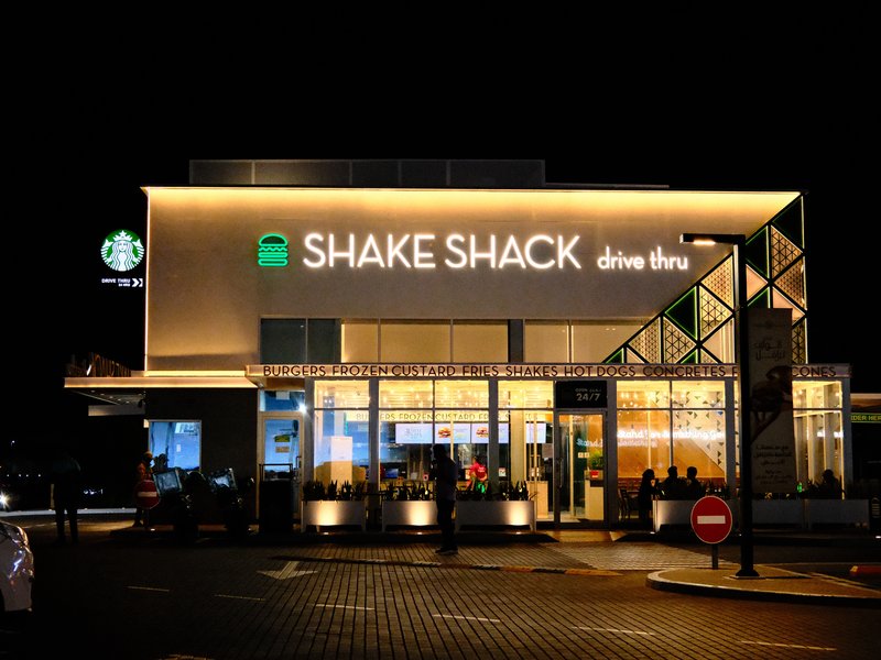 Night view of a Shake Shack restaurant with bright signage and a Starbucks nearby.