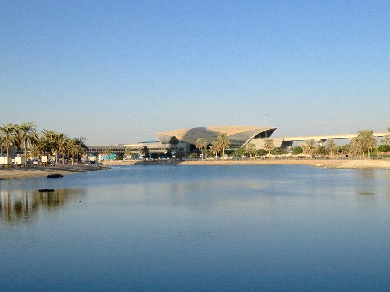 A serene view of a calm water body reflecting a clear blue sky and modern architecture in the background.