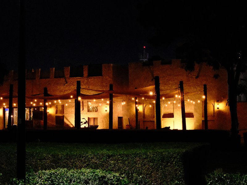 A warmly lit outdoor venue at night with string lights and a castle-like structure.