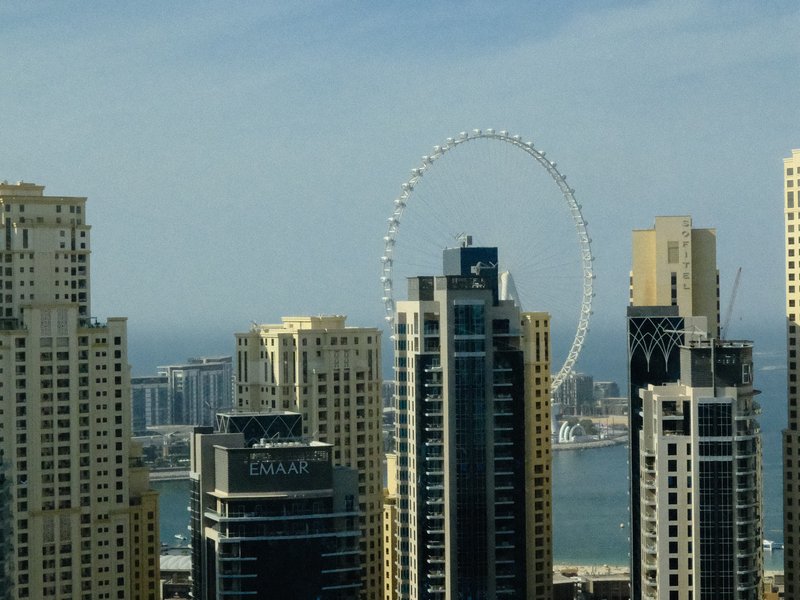 A view of modern skyscrapers with a large Ferris wheel in the background against a clear sky.