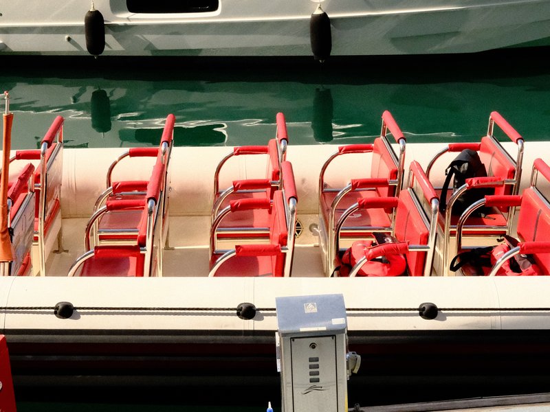 A close-up view of red seats in a boat docked at a marina, with green water in the background.