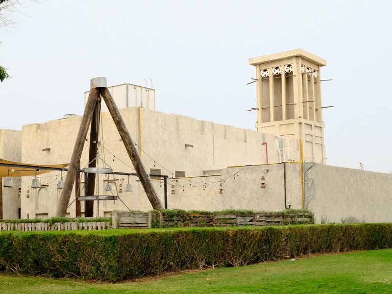 A traditional building with a wind tower, surrounded by greenery and a wooden structure in the foreground.