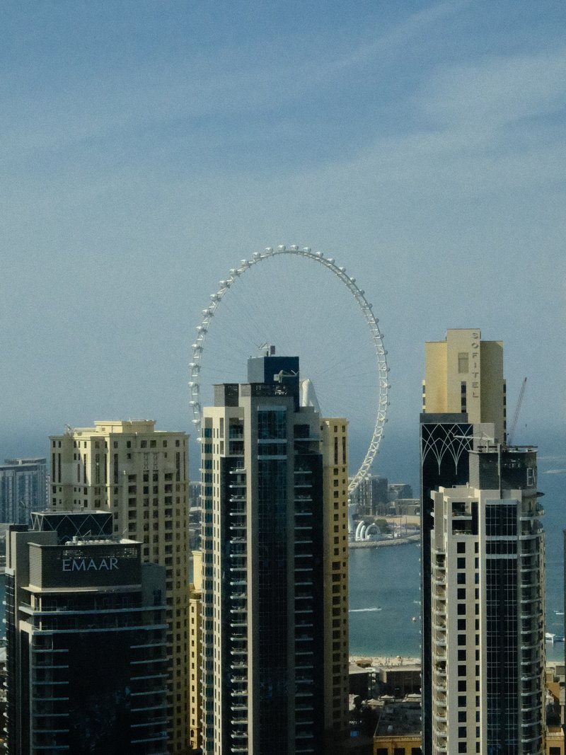A skyline view featuring tall buildings with a large Ferris wheel in the background against a blue sky.