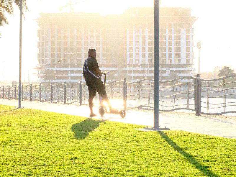 A person riding a scooter on a grassy path with a building in the background during golden hour.
