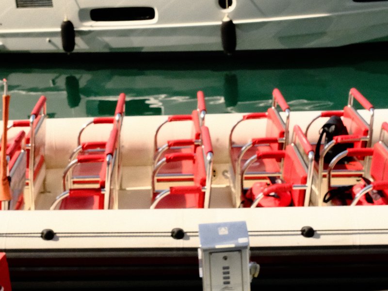 A close-up view of empty red and white boat seats on a docked boat, with turquoise water in the background.