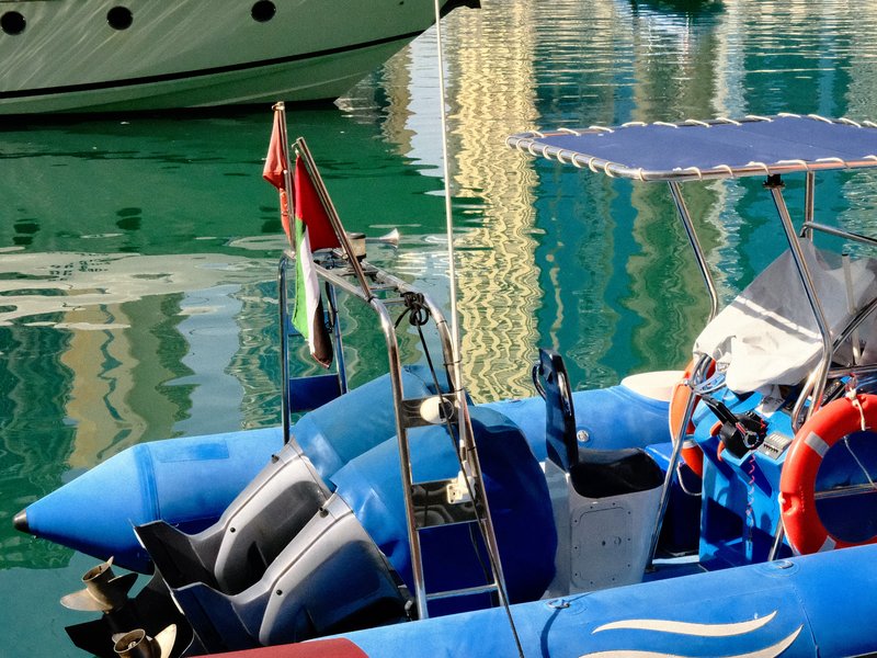 A blue boat with a canopy docked in a marina, reflecting colorful buildings in the water.