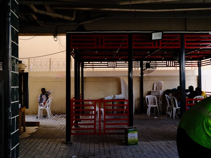 A dimly lit indoor space with red structures and people seated in plastic chairs.
