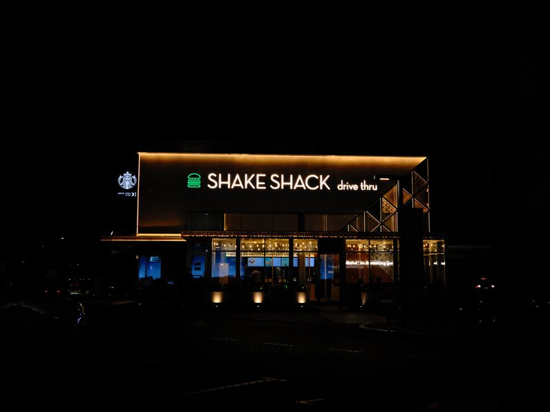 Night view of a Shake Shack restaurant illuminated with neon lights and warm glow.