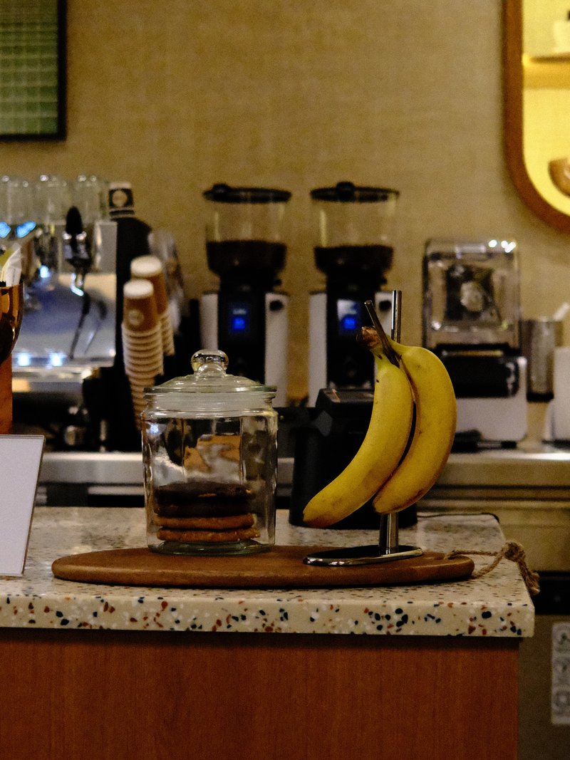 A cozy café scene featuring a glass jar of coffee and two bananas on a wooden tray.