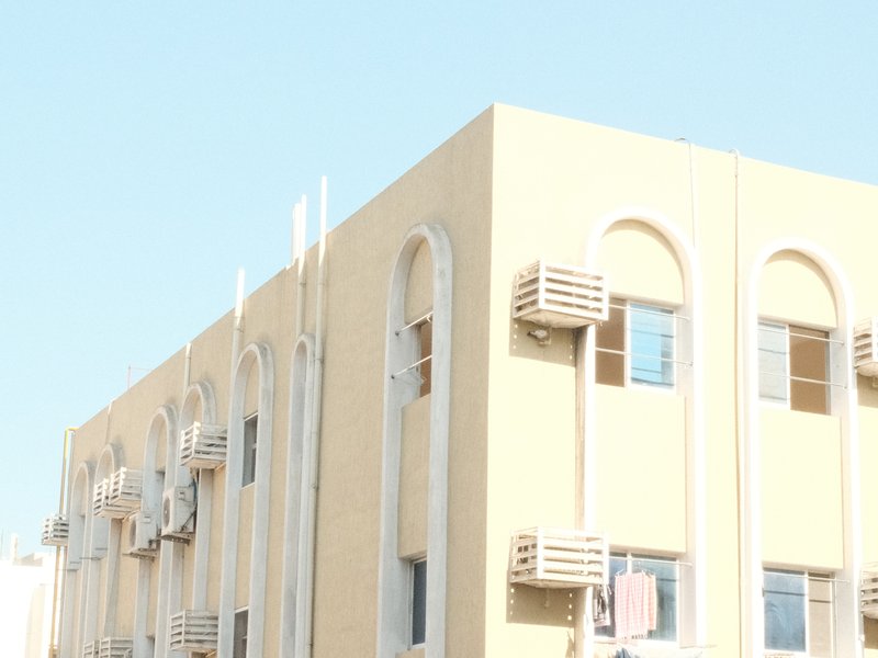 A light-colored building with air conditioning units on the exterior against a clear blue sky.