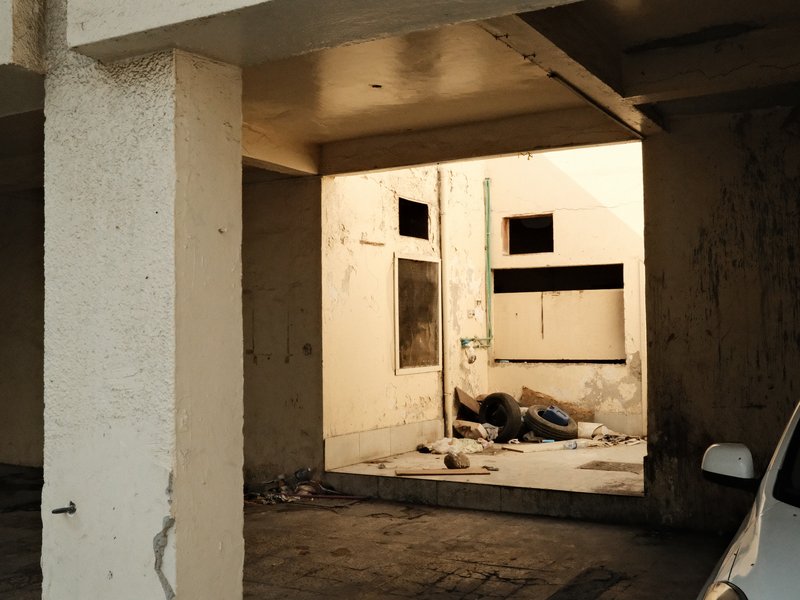 A dimly lit urban space with a person lying on the ground, surrounded by debris and peeling walls.