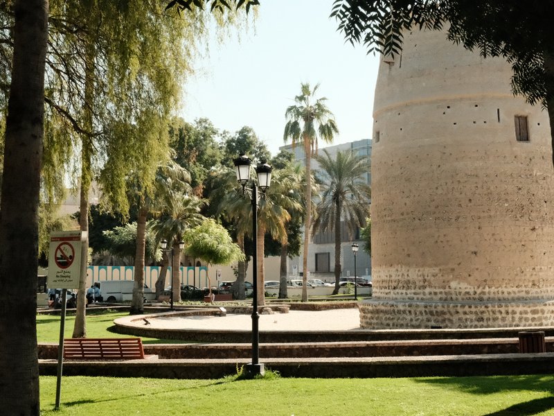 A historic tower surrounded by palm trees and green grass in a sunny park setting.