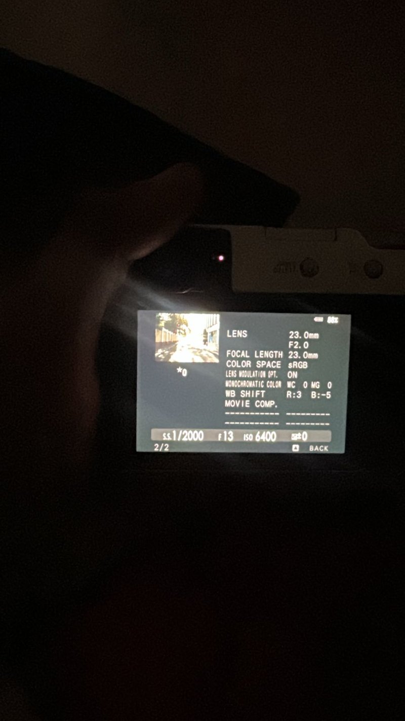 A hand holding a camera displaying settings on the screen in low light.