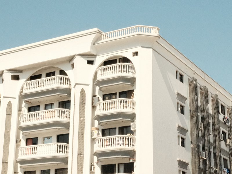 Close-up of a modern apartment building with white facade and balconies against a clear blue sky.