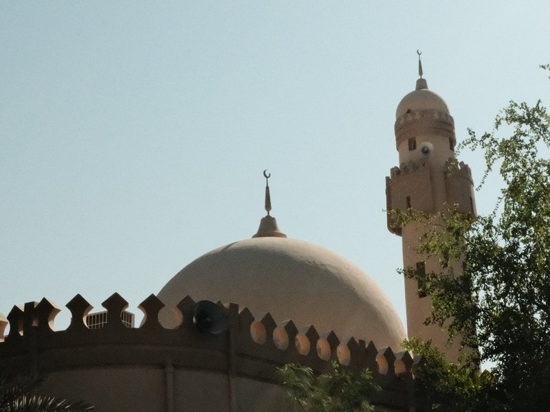 A close-up view of a mosque's dome and minaret against a clear sky.