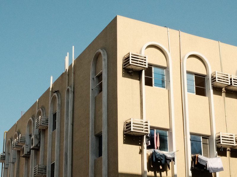 Close-up of a yellow building with air conditioning units and hanging laundry against a clear blue sky.