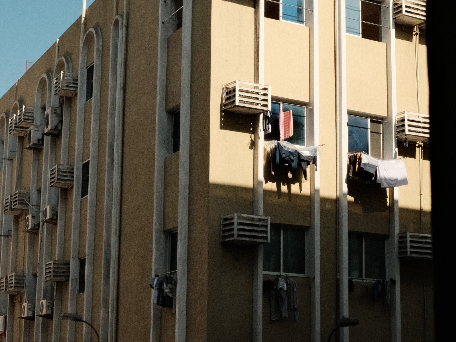A beige building with air conditioning units and laundry hanging from windows under bright sunlight.