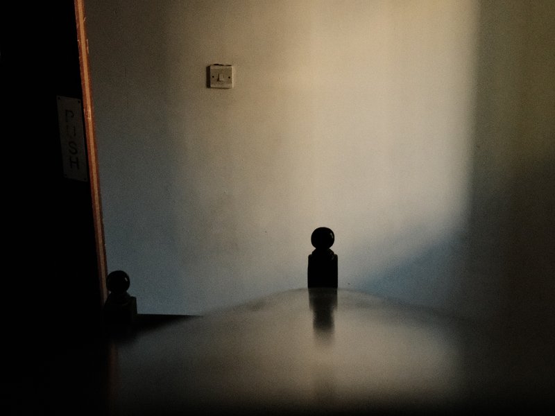 A dimly lit room with a wooden table and shadowy walls, creating a mysterious atmosphere.