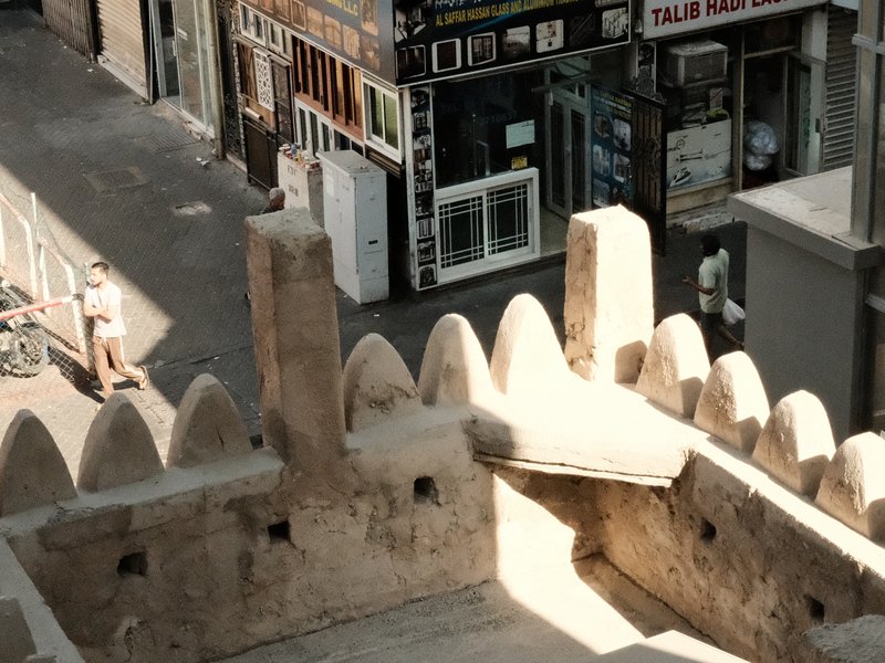 View from a historic building showing a street with shops and pedestrians in a sunny urban setting.