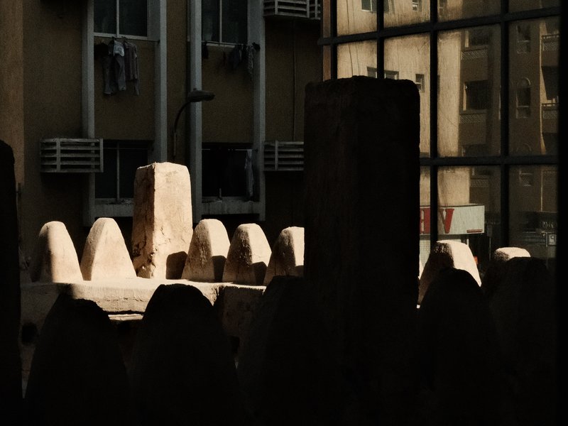 Silhouetted stone structures in an urban setting with reflections from glass buildings.