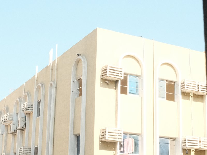 A light-colored building with air conditioning units and blue sky in the background.
