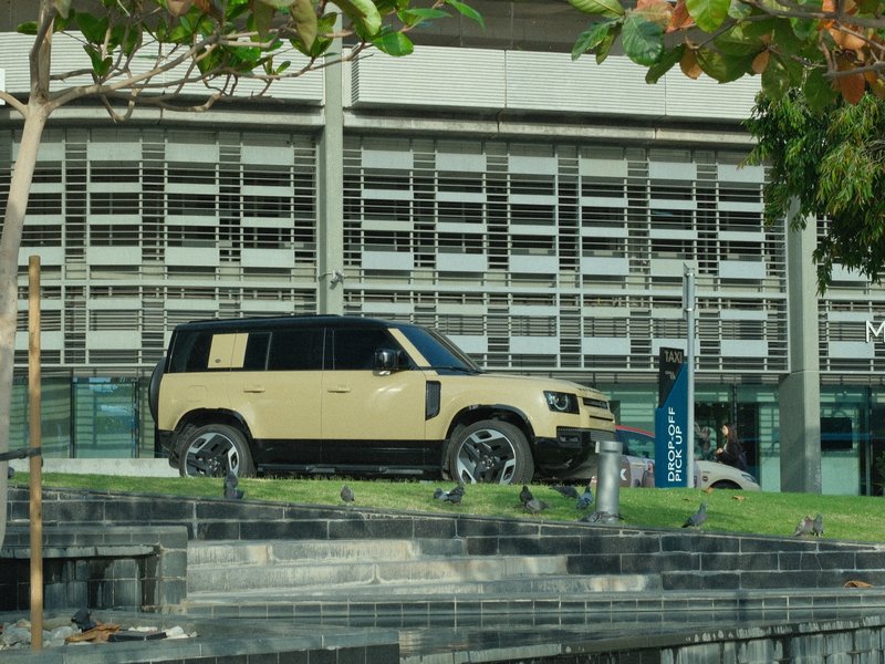 A beige SUV parked on a grassy area next to a modern building with large windows.