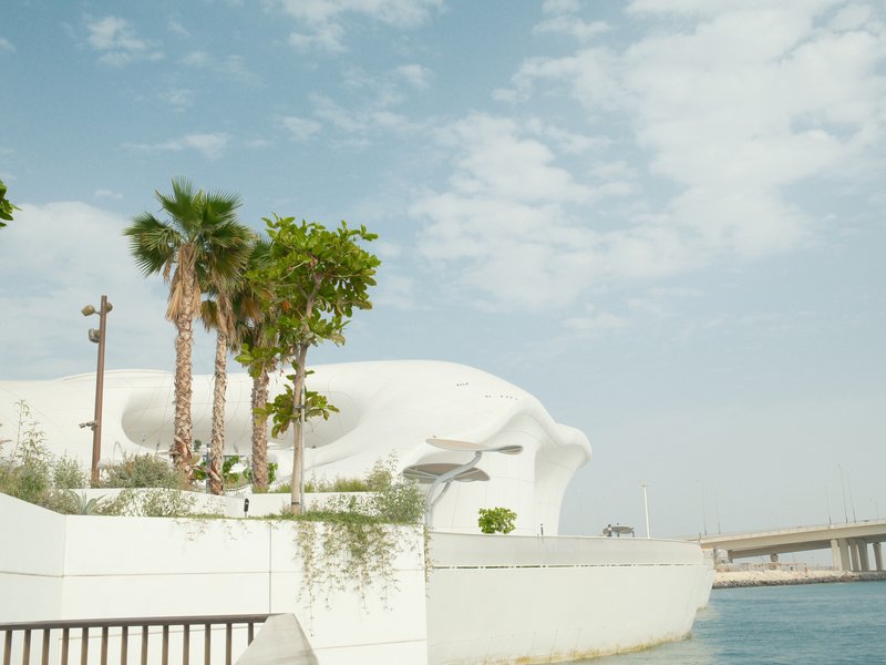 Modern architectural structure beside a body of water with palm trees and a cloudy sky.