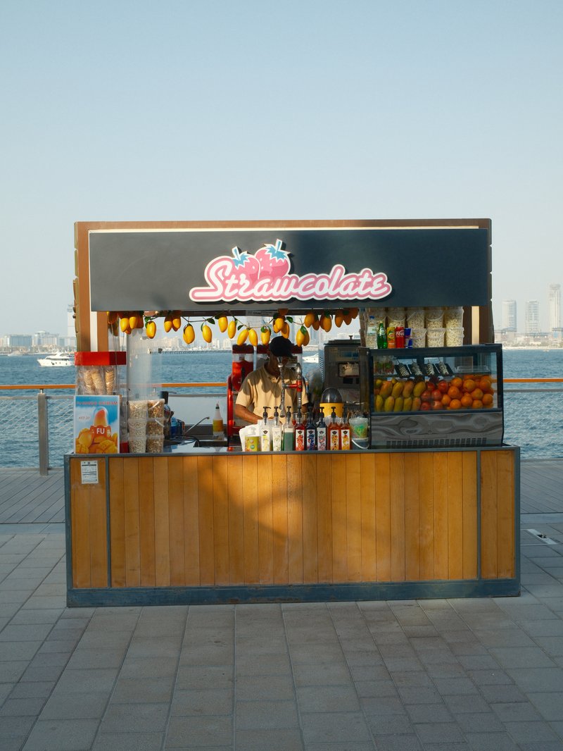 A colorful outdoor juice stand by the water, featuring fresh fruits and drinks.