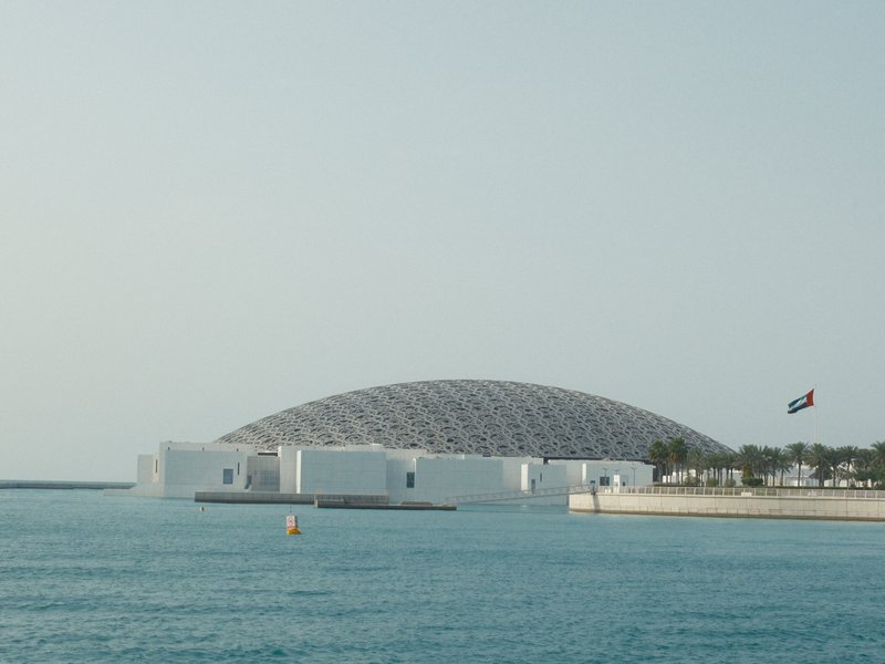 A modern architectural structure with a dome, surrounded by water and a clear sky.