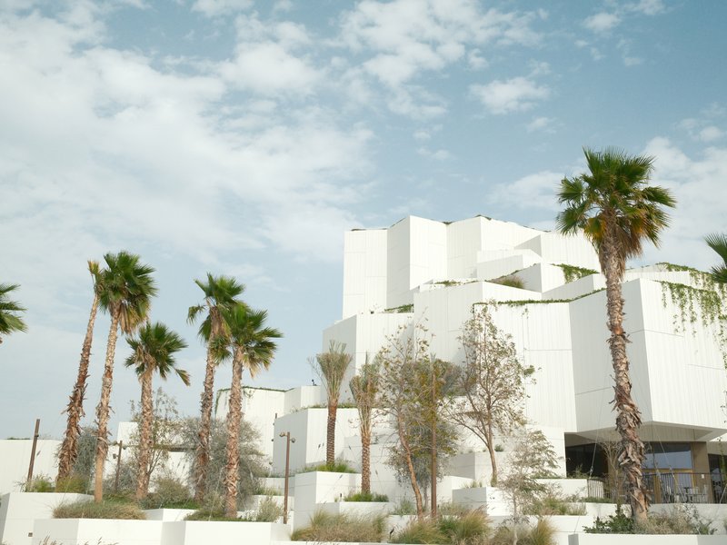 Modern white architecture surrounded by palm trees under a partly cloudy sky.
